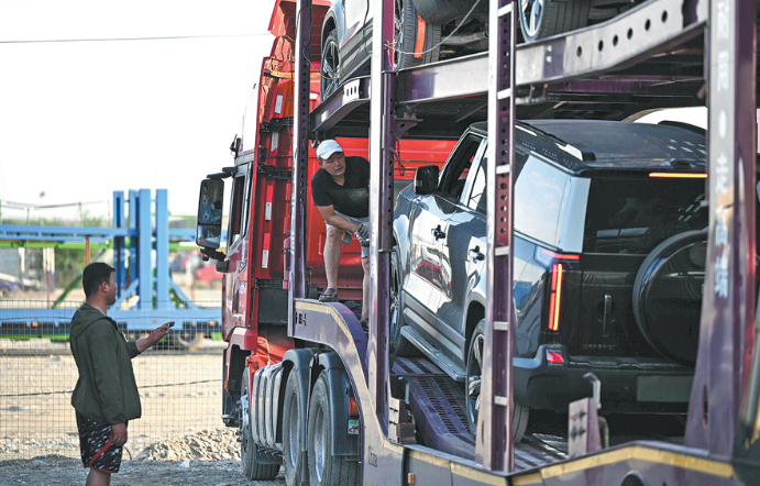 Employees load vehicles imported from China onto a truck at a logistics center in Zharkent, Kazakhstan, on May 22. LI RENZI/XINHUA